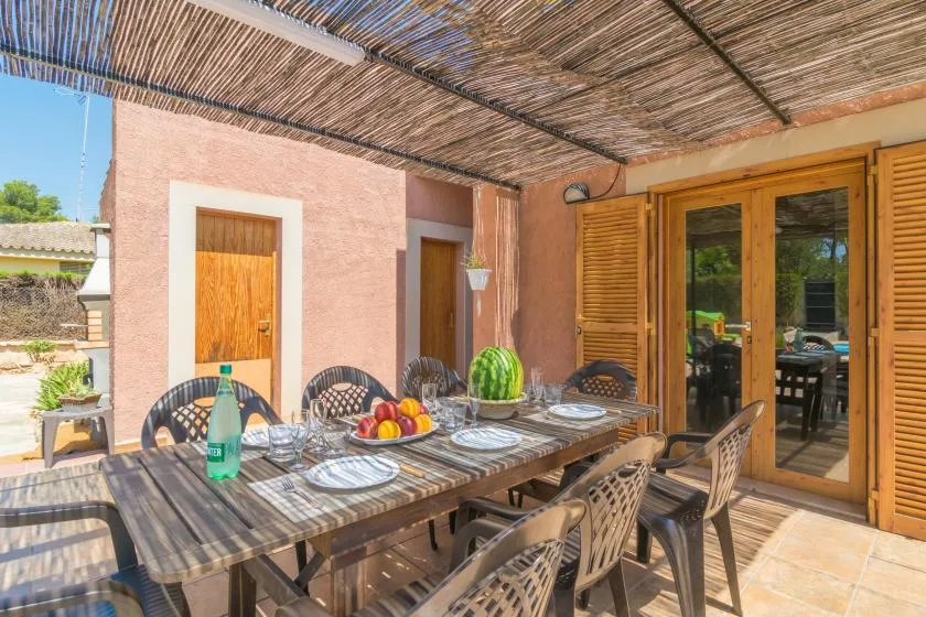A shaded outdoor dining area with a long table set beneath a reed canopy.