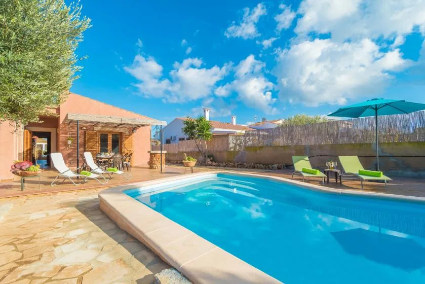 An outdoor swimming pool beside a patio with loungers and a large umbrella.