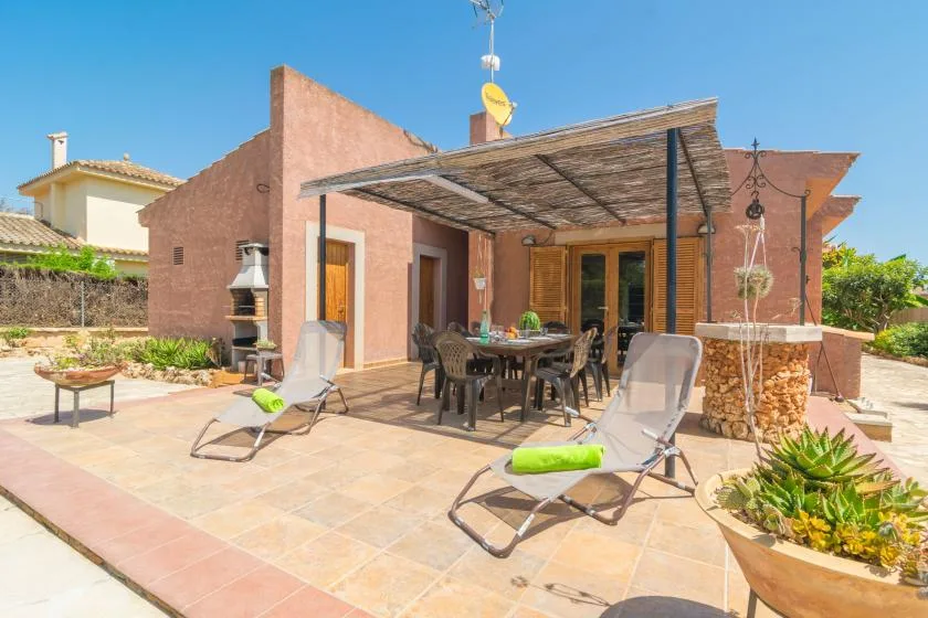 A sunny stone patio with outdoor seating beneath a shaded pergola.