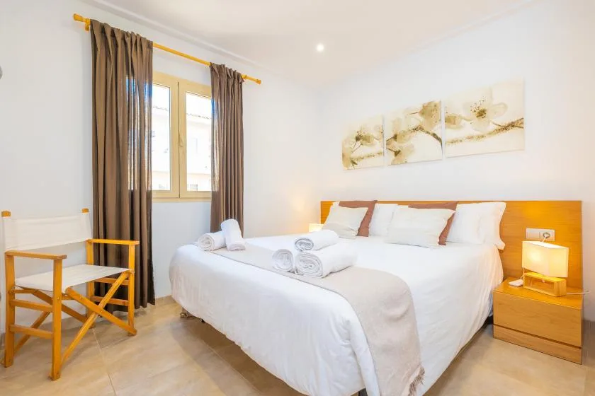 Un dormitorio luminoso con una cama tendida, una mesita de noche y una ventana con cortinas.