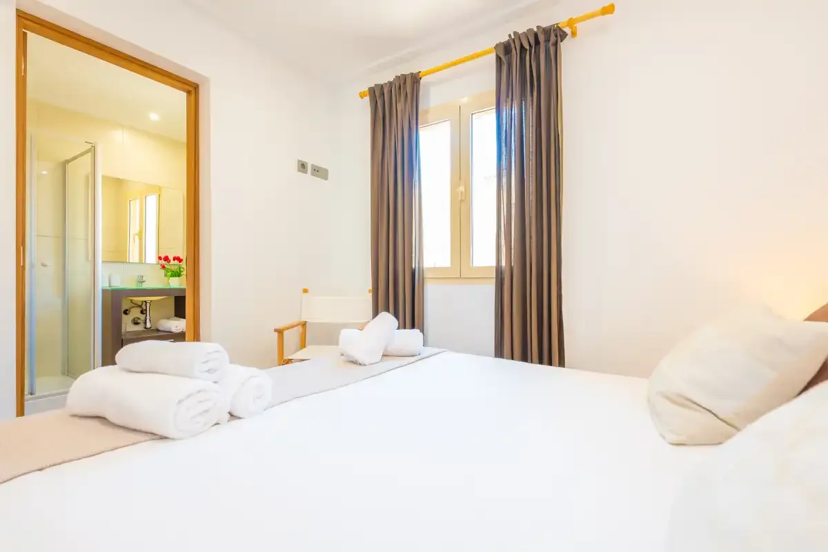 Dormitorio con una cama tendida y una ventana con cortinas oscuras.