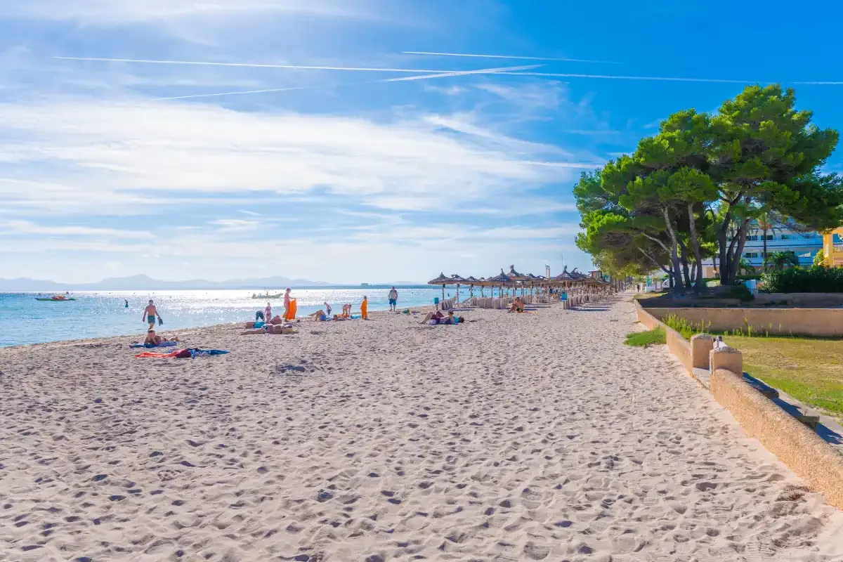 Una playa de arena se extiende junto a aguas azules y tranquilas bajo un cielo despejado.