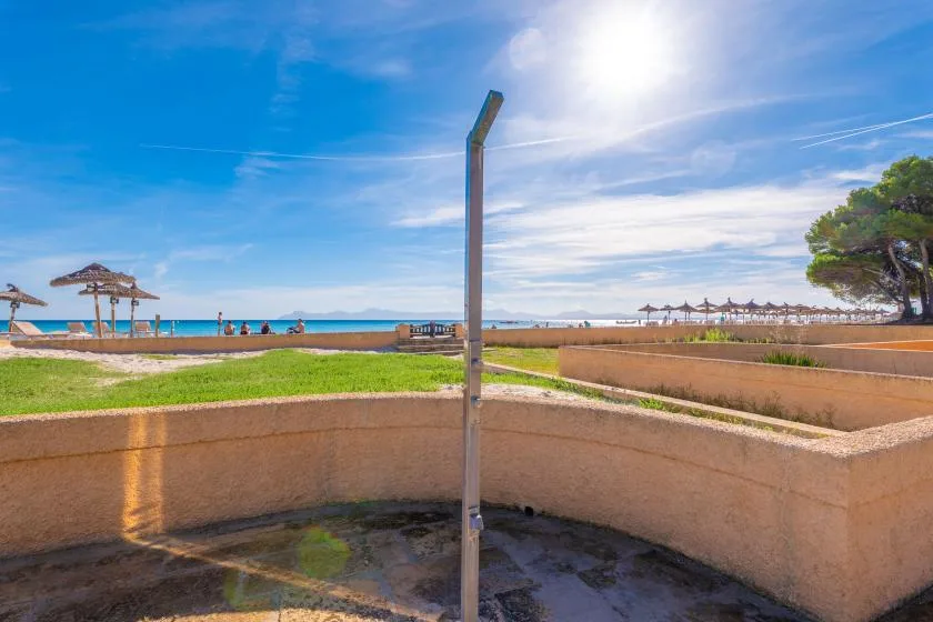 Una playa soleada con un muro bajo y sombrillas junto a la orilla.