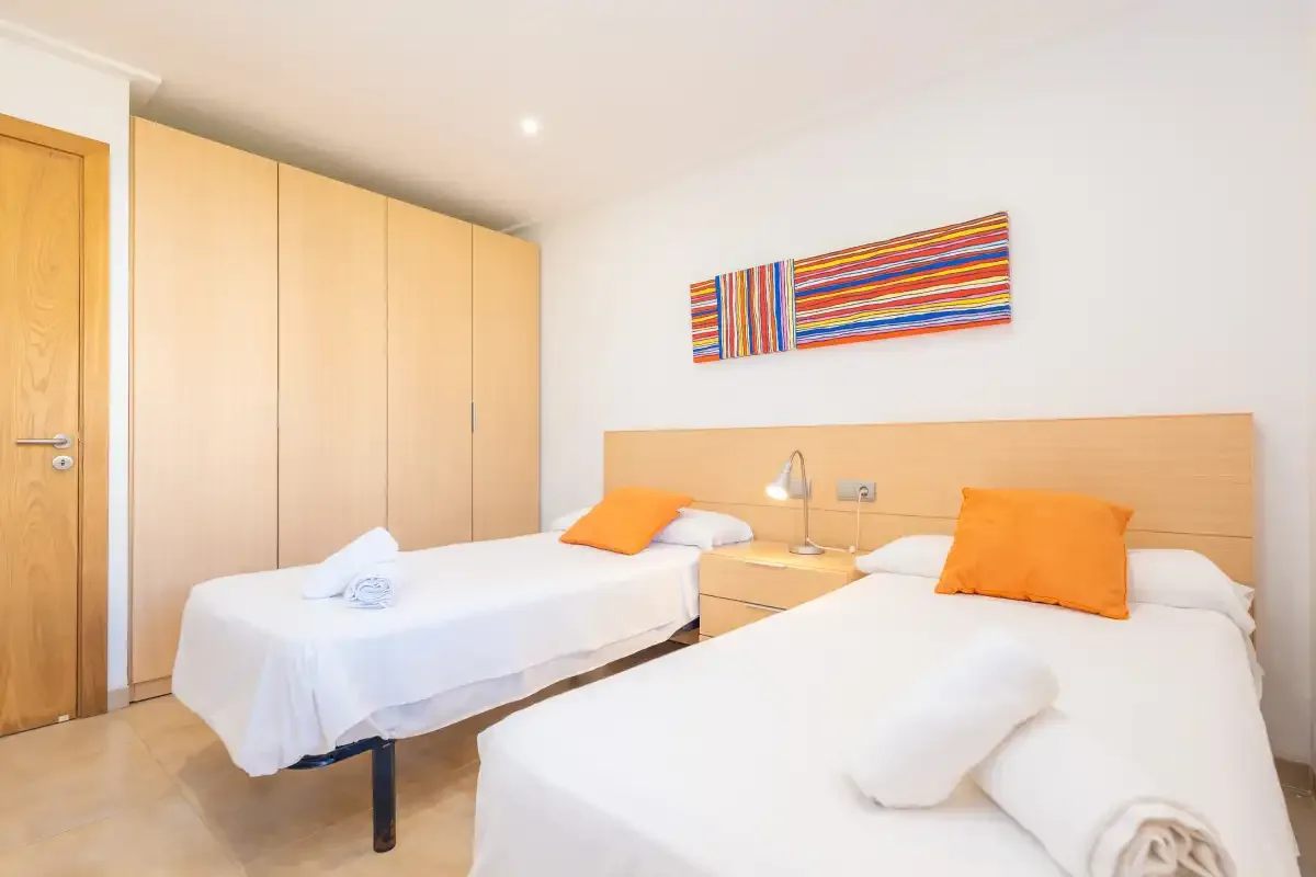 Dormitorio con dos camas, armarios de madera clara y arte colorido en la pared.