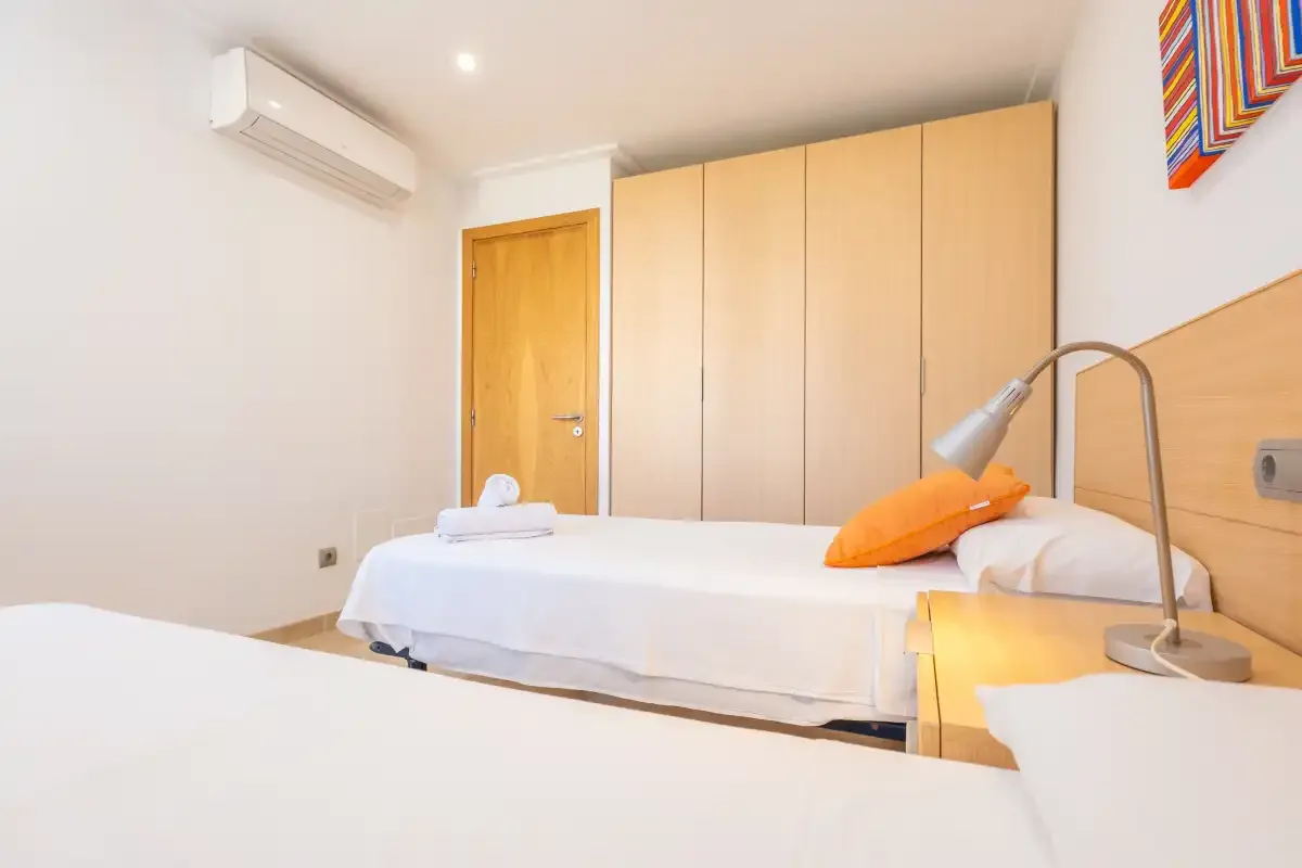Un dormitorio con dos camas, armarios de madera clara y una lámpara de noche.