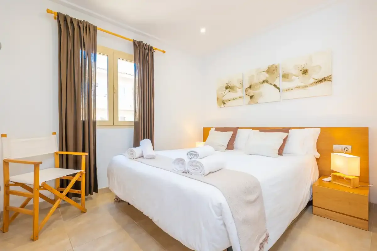 Un dormitorio luminoso con una cama bien hecha y una ventana con cortinas.