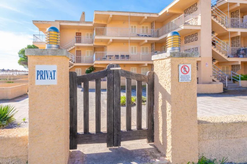 Un edificio de apartamentos se alza tras una puerta de madera oscura en un patio soleado.