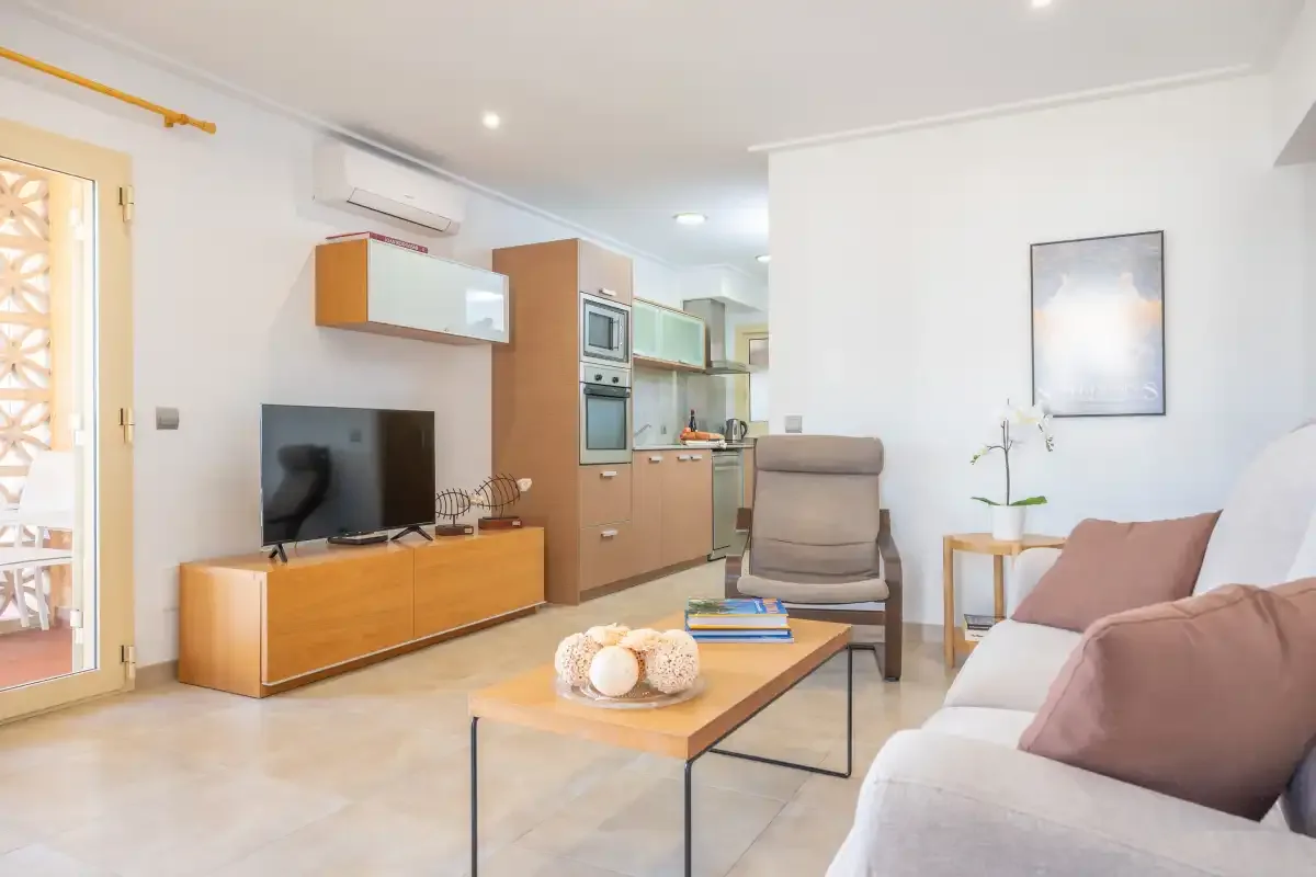 Una sala de estar luminosa con asientos, un televisor y una cocina abierta.