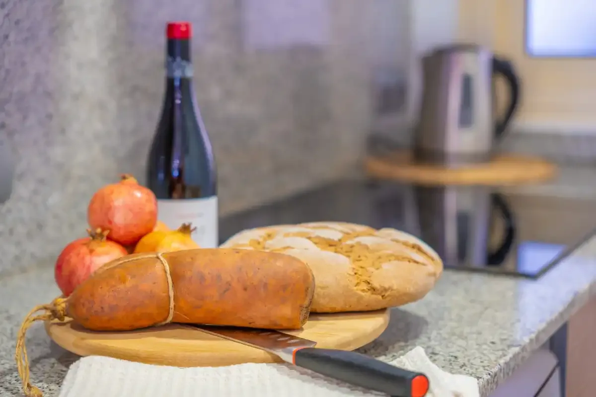 Una encimera de cocina muestra pan, fruta y una botella junto a una placa de cocina.
