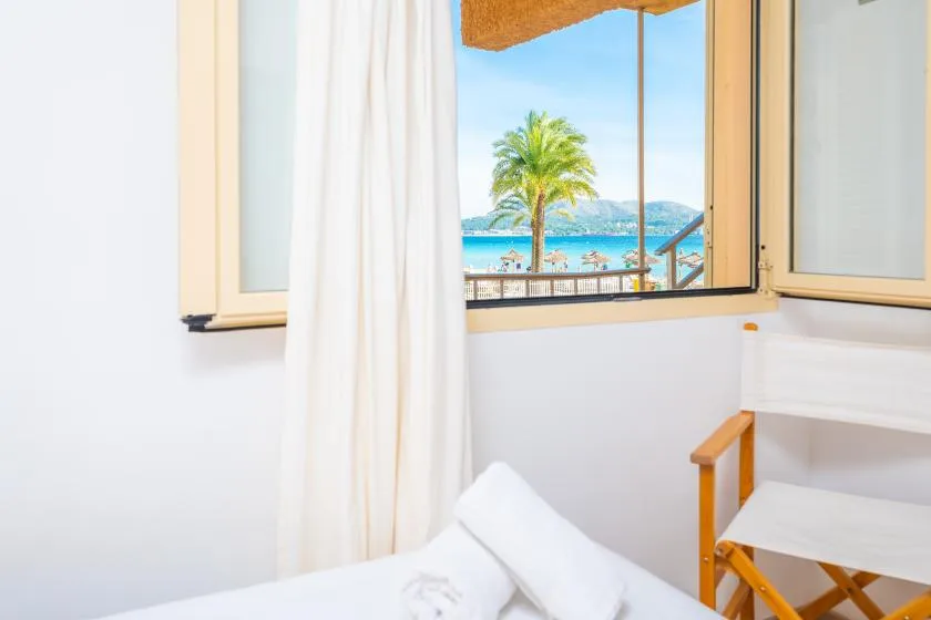 Un dormitorio luminoso con una cama junto a una ventana abierta con vistas al mar.