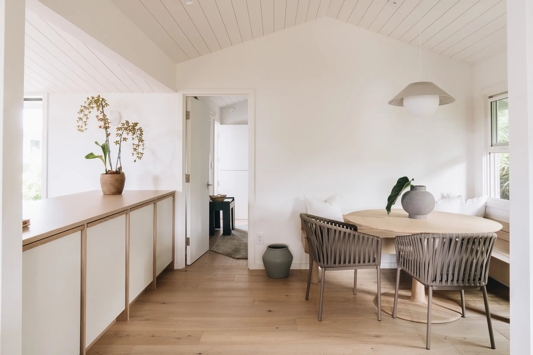 A bright dining area with a round table, woven seating, and a potted plant.