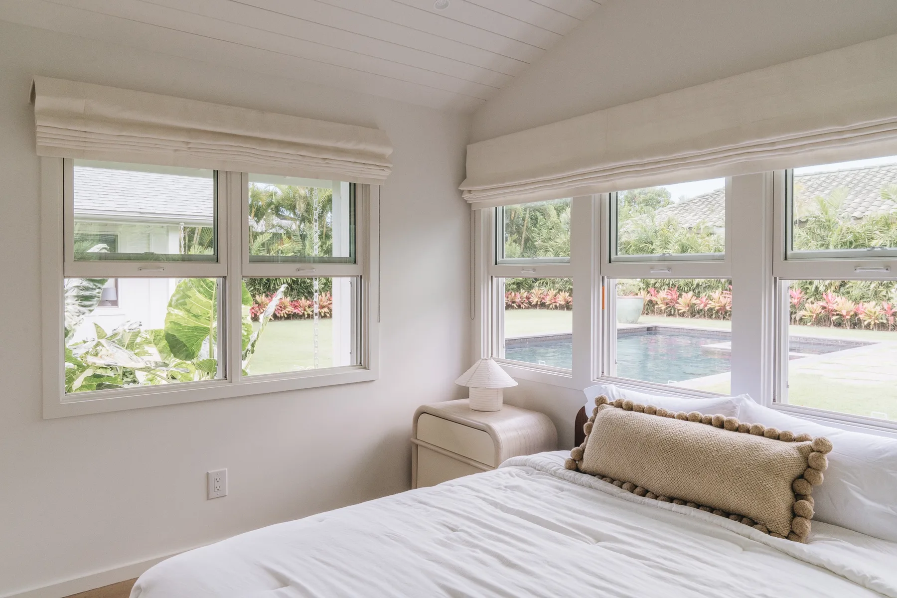 A bright bedroom with a neatly made bed and large windows overlooking a pool.