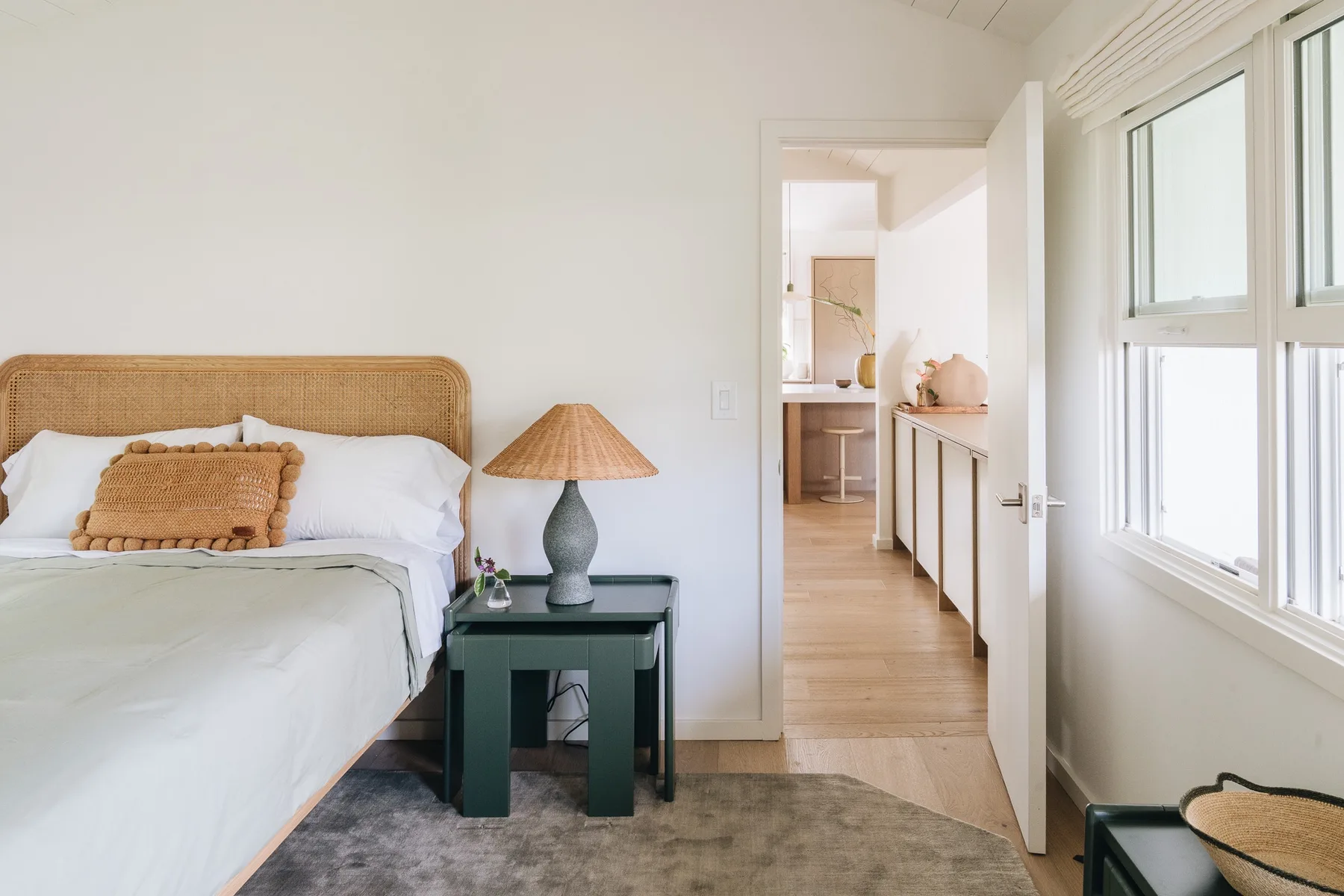 A bright bedroom with a bed beside an open doorway leading to a small kitchenette.