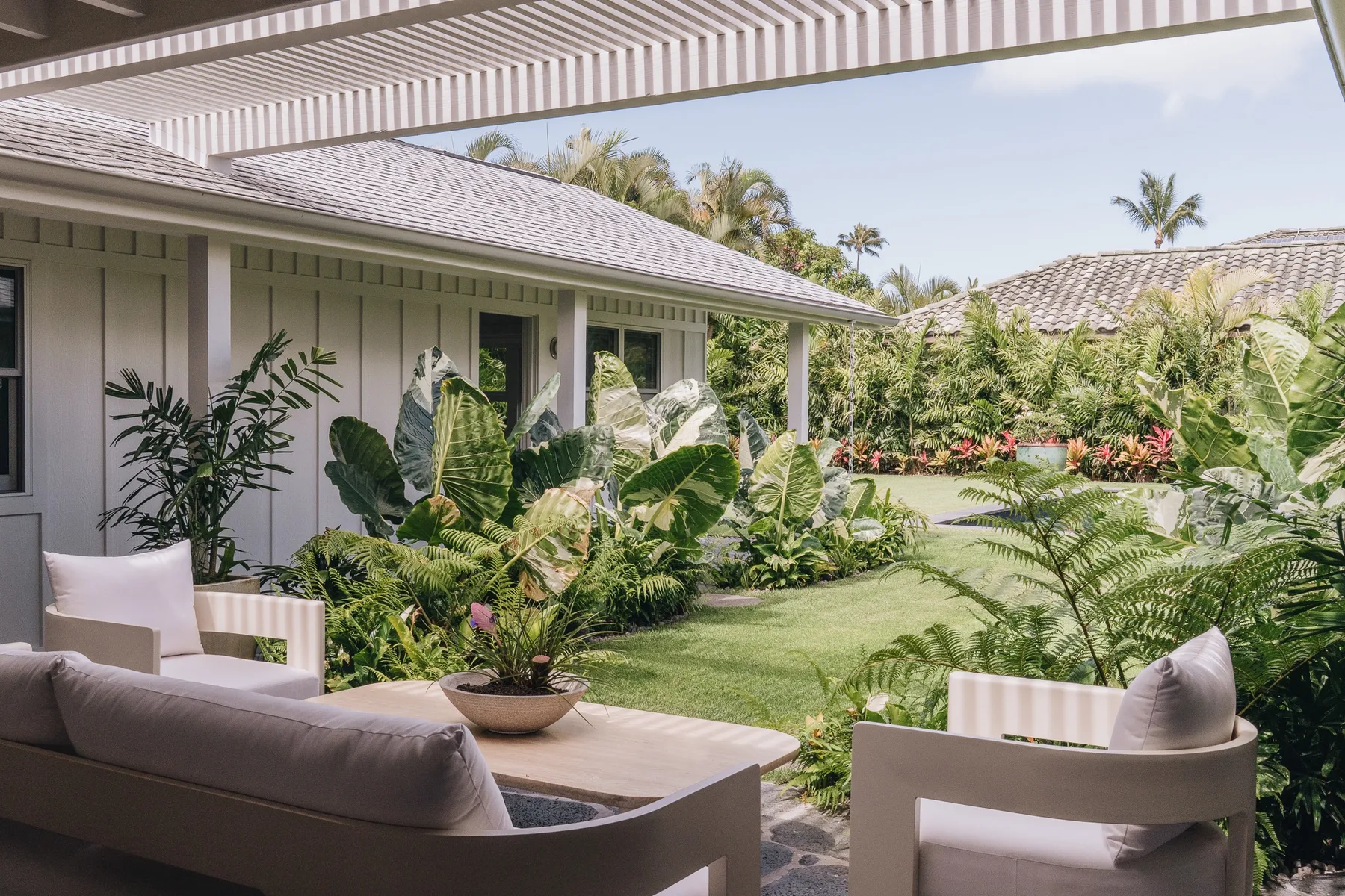 A covered patio with outdoor seating overlooks a green garden.