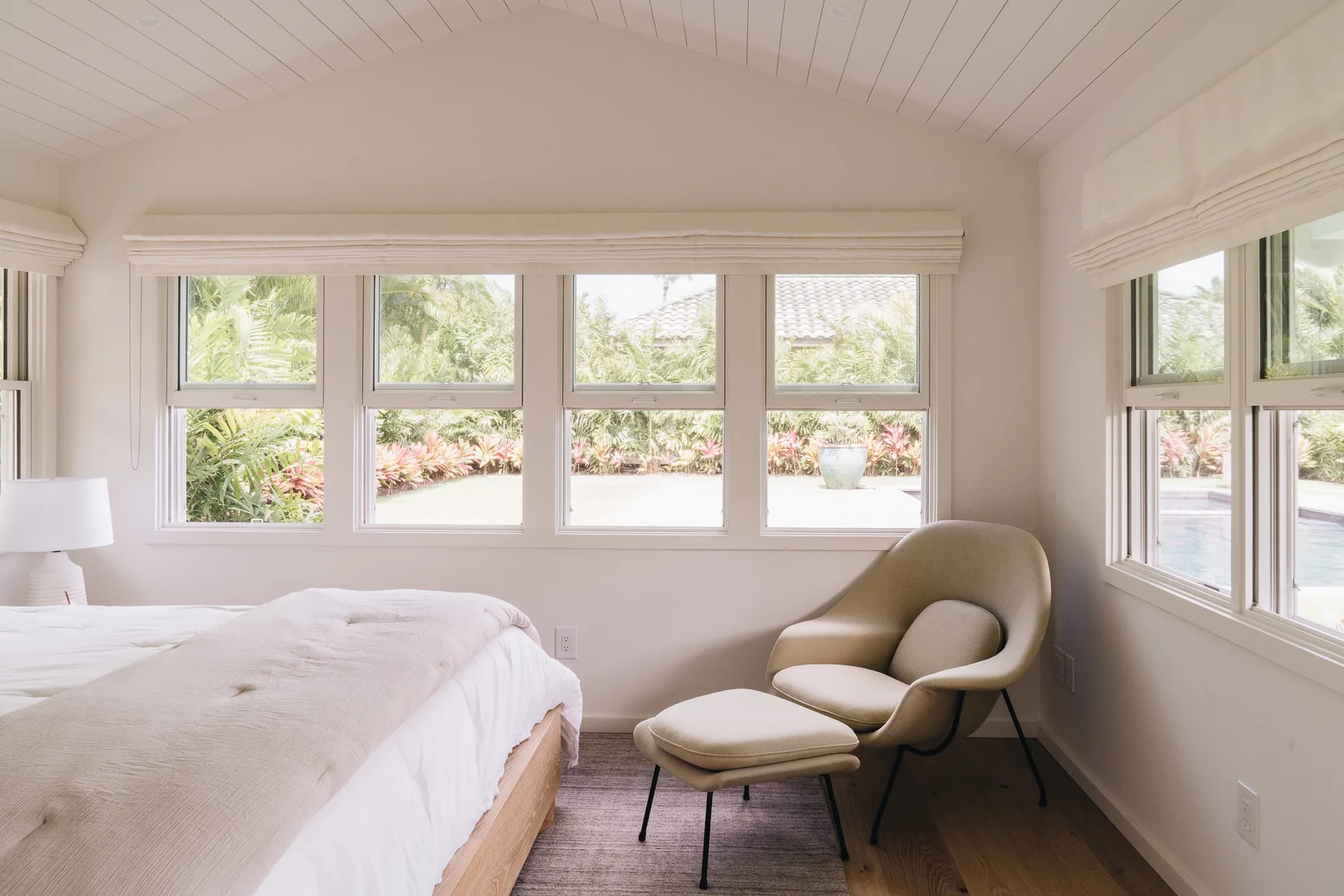 A bright bedroom with a bed, an upholstered chair, and wide windows.