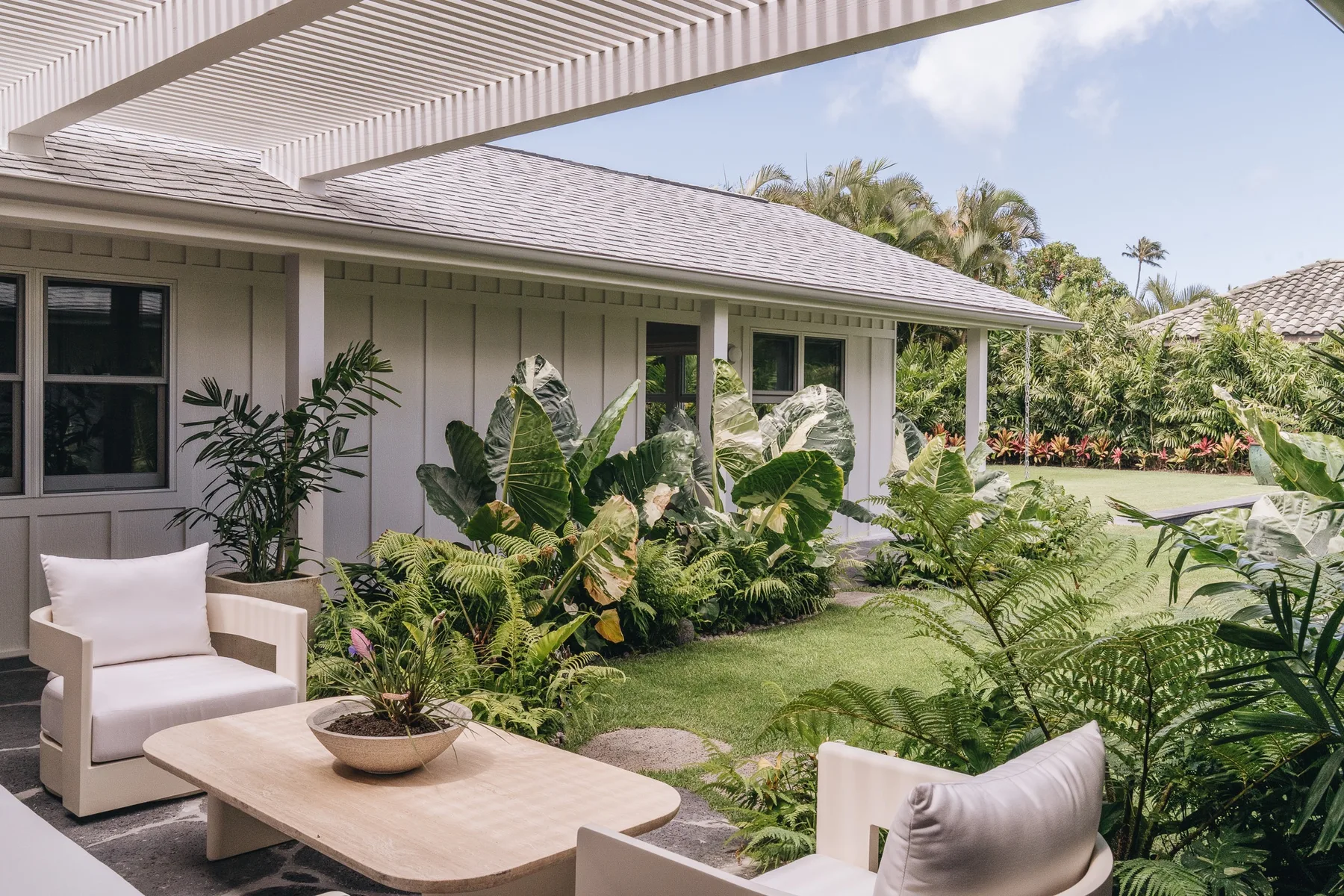 A covered outdoor seating area overlooks a garden with lush tropical plants.