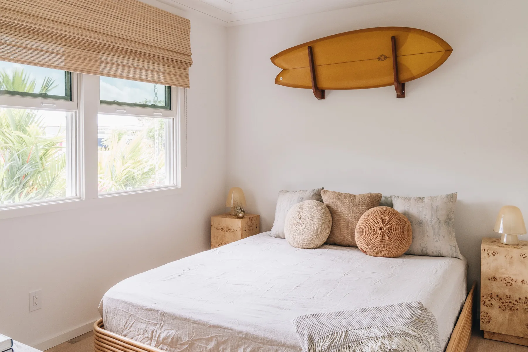 A bright bedroom with a bed beneath a wall-mounted surfboard.