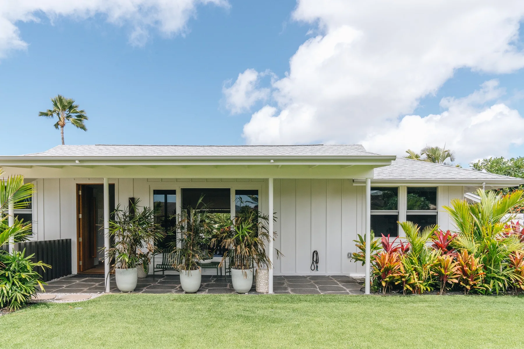 A single-story house with a covered patio, potted plants, and a lawn.
