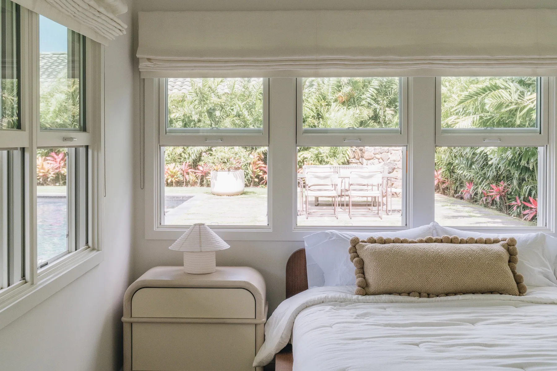 A bright bedroom with a bed beside large windows overlooking a garden.
