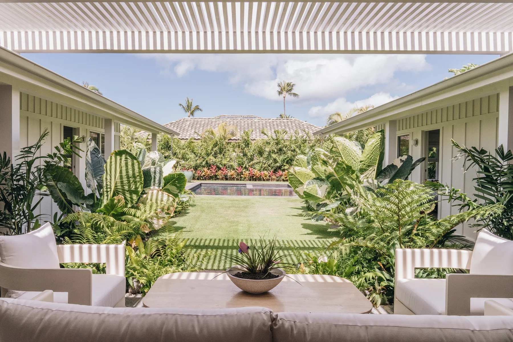 A covered patio seating area overlooks a garden and a small pool.