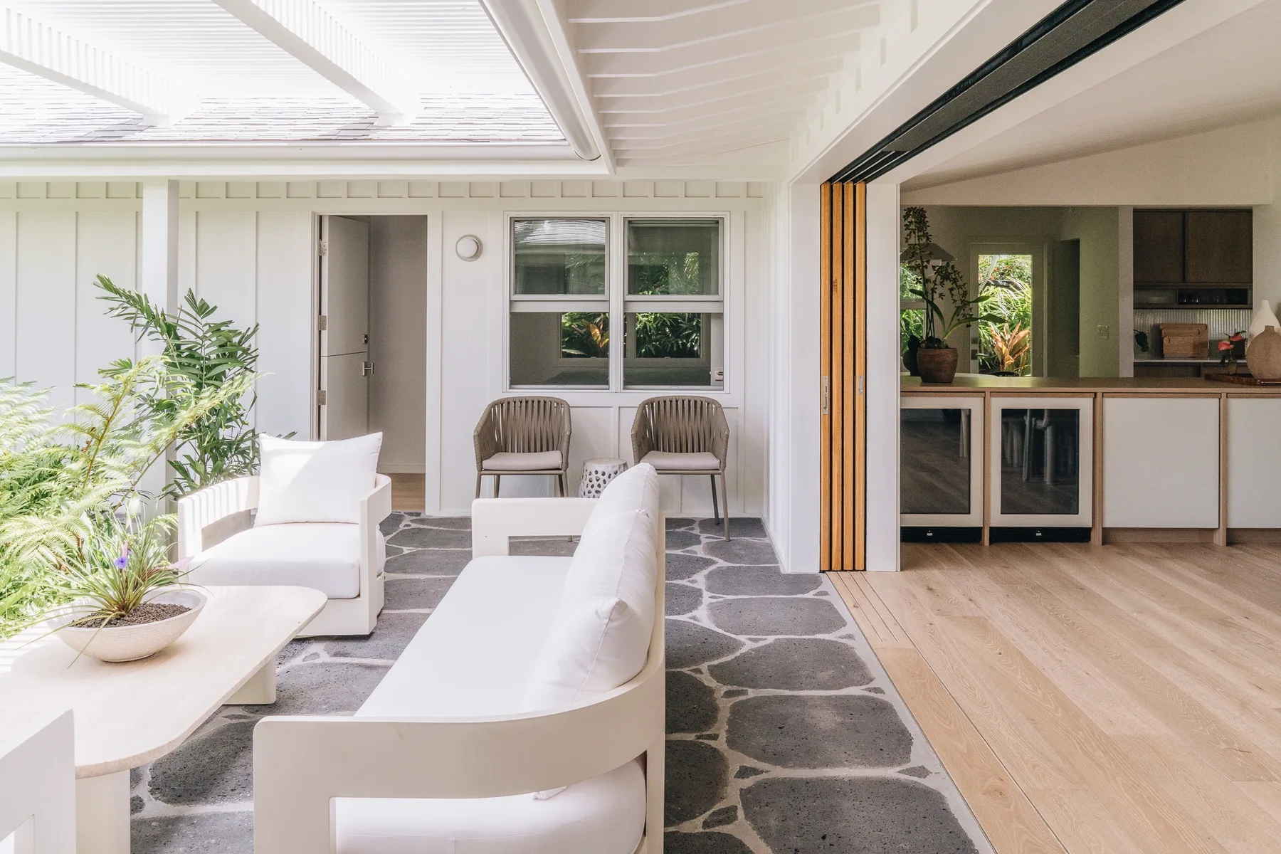 A bright patio seating area opens onto a kitchen, with plants beside the seating.