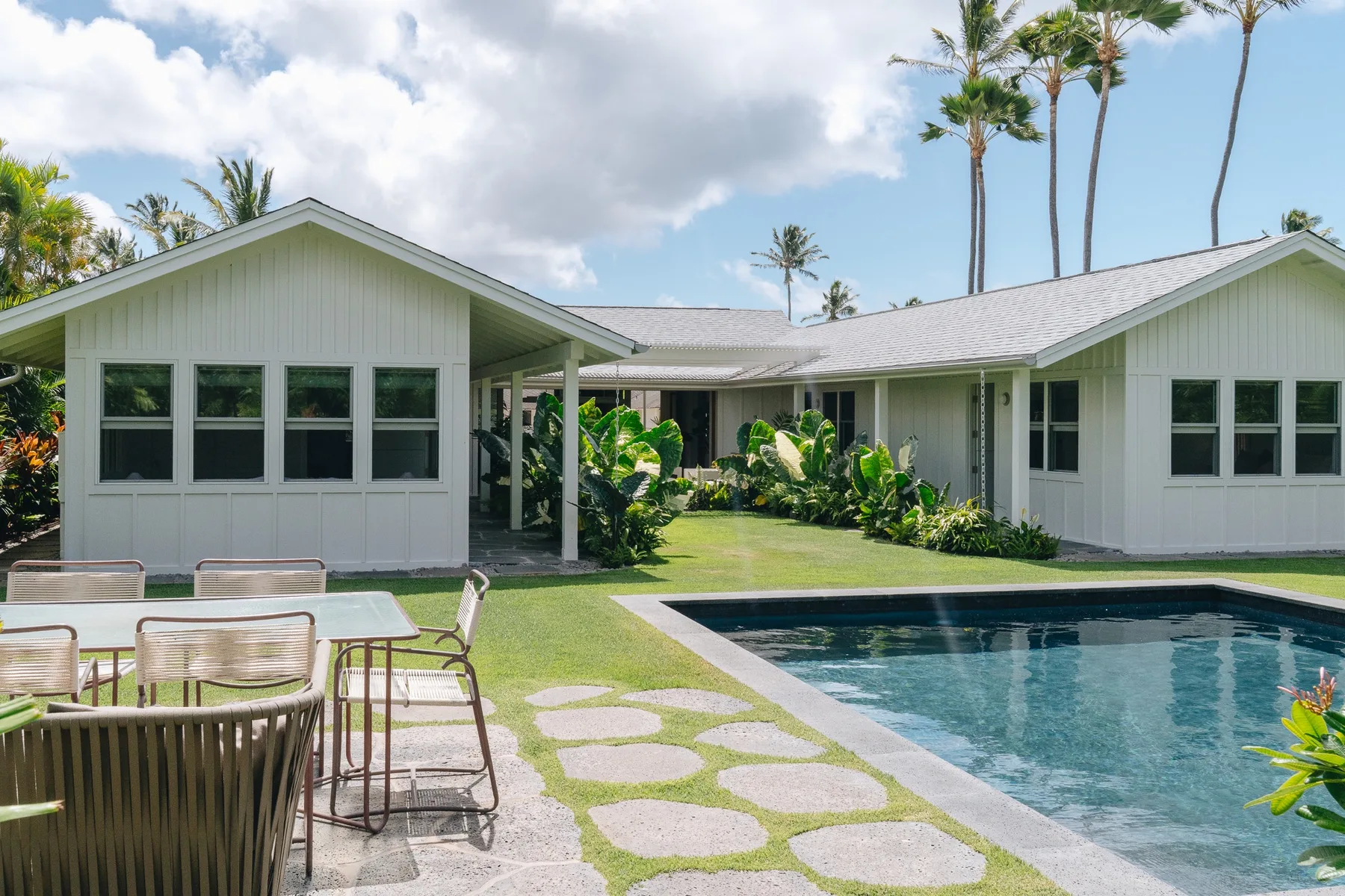 A single-story house faces a swimming pool, with patio seating and stepping stones in the yard.