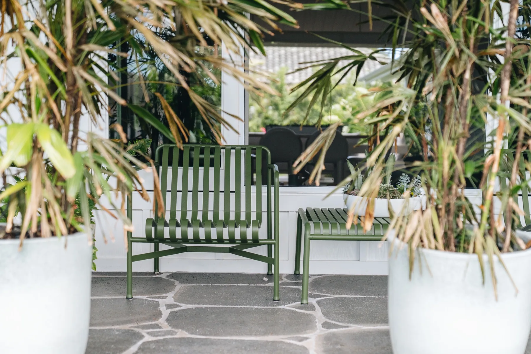 A patio seating area with green chairs, partly screened by potted plants.