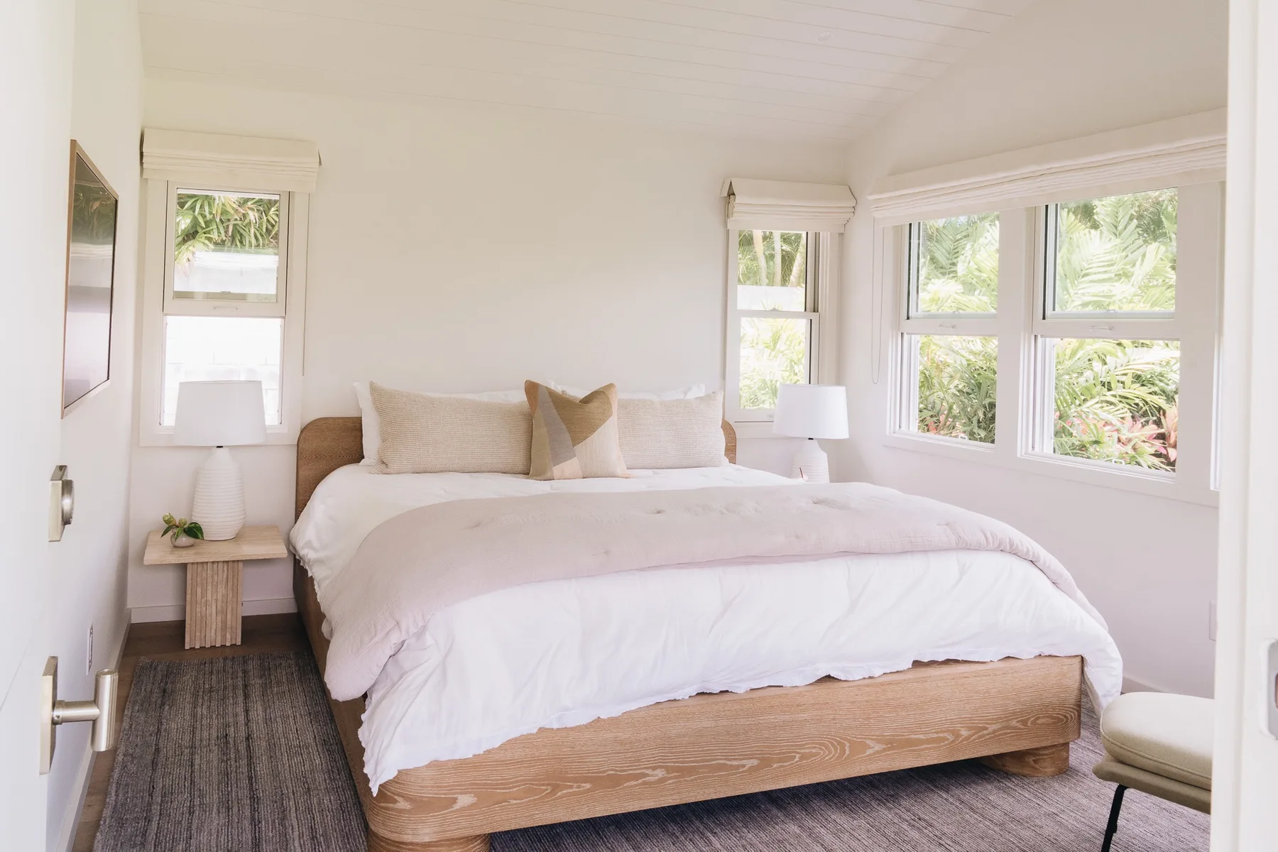 A bright bedroom with a bed and large windows overlooking greenery.
