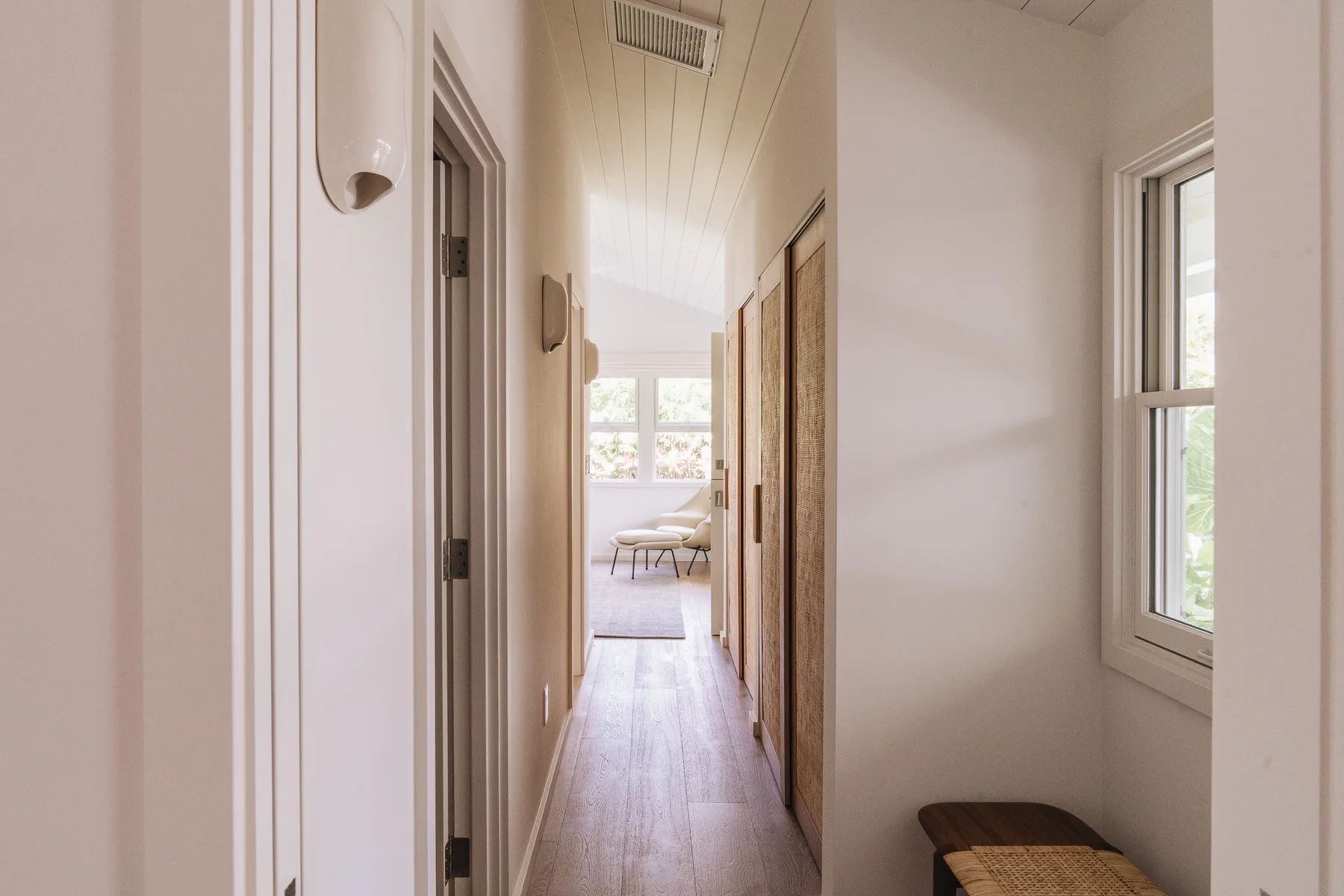 A bright hallway with wood flooring and a window at the far end.