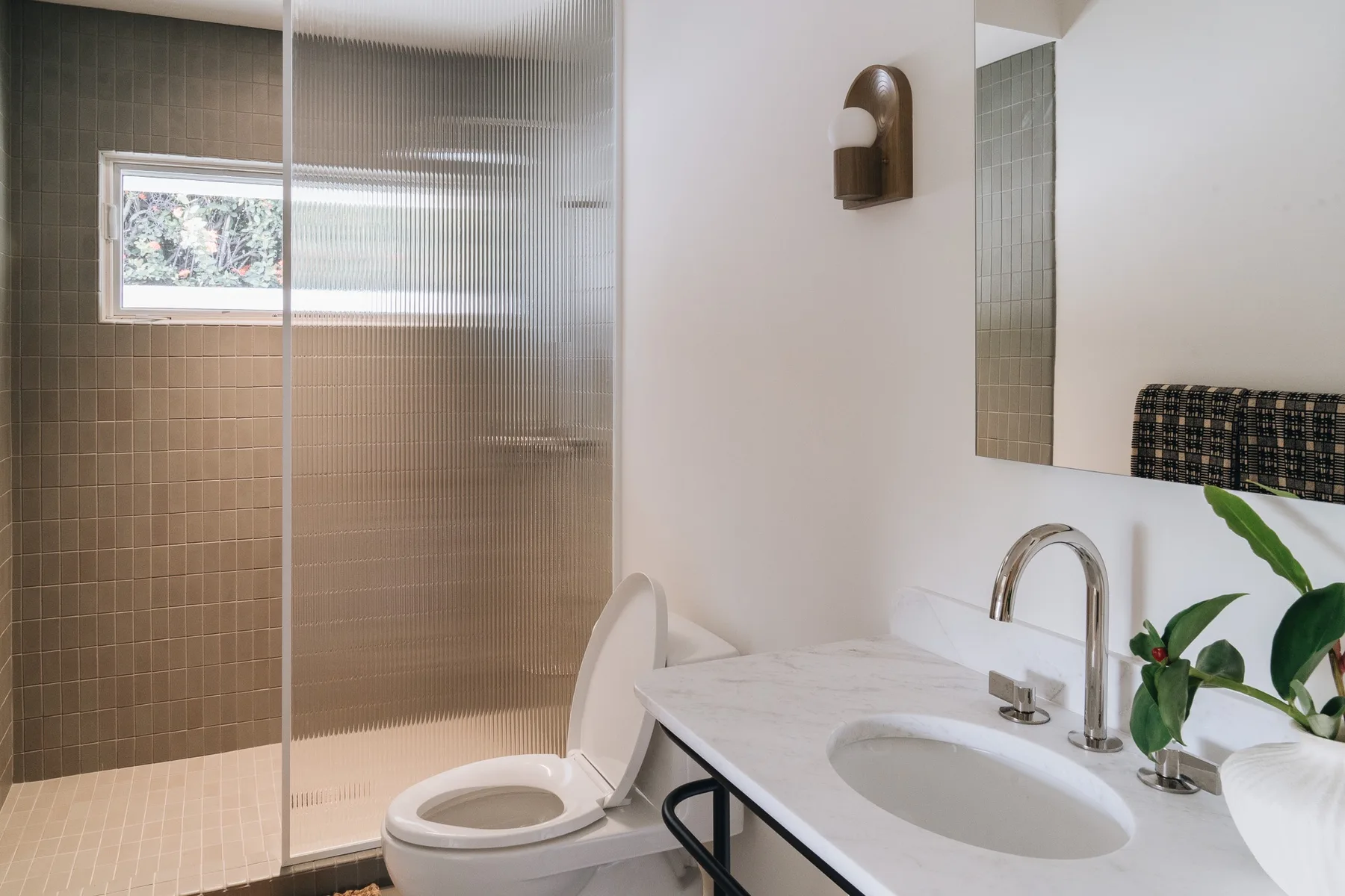 A bright bathroom with a sink, toilet, and tiled shower area.