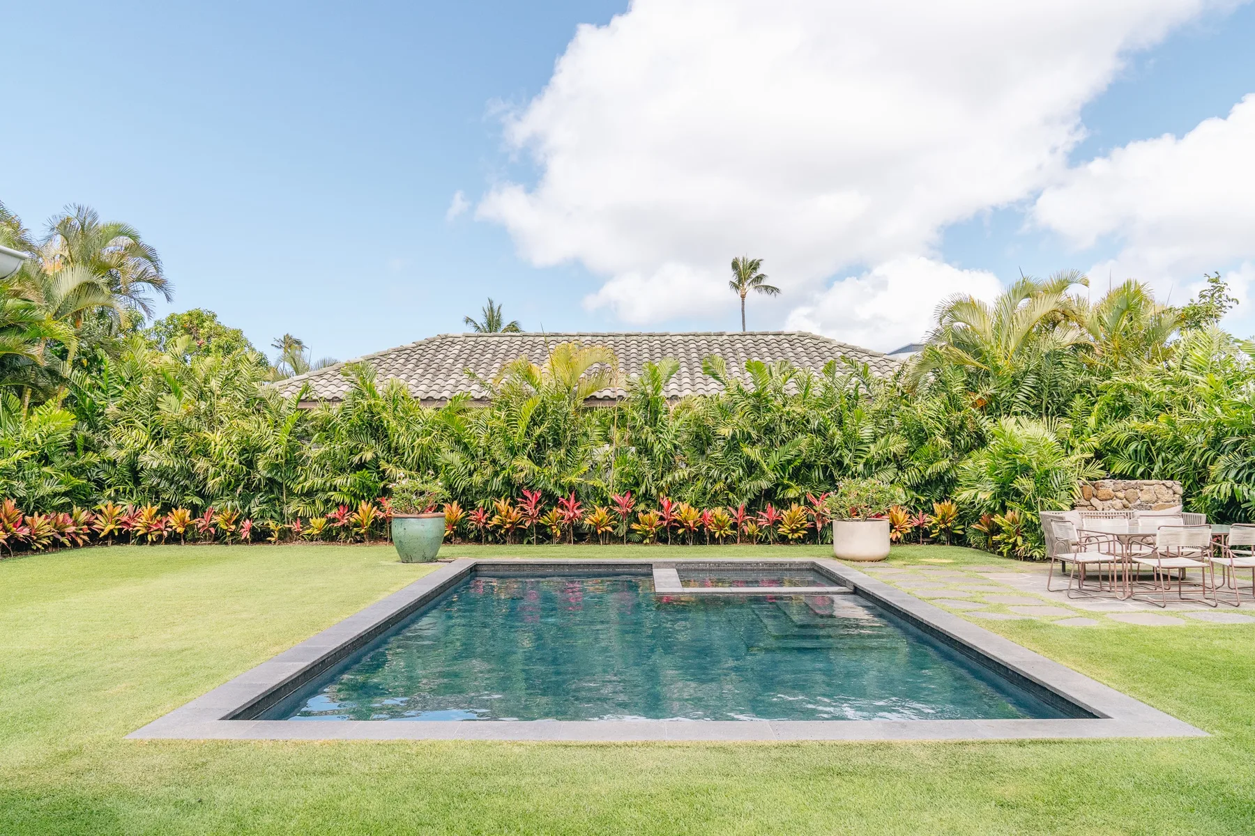 An outdoor swimming pool is surrounded by a lawn and lush garden.