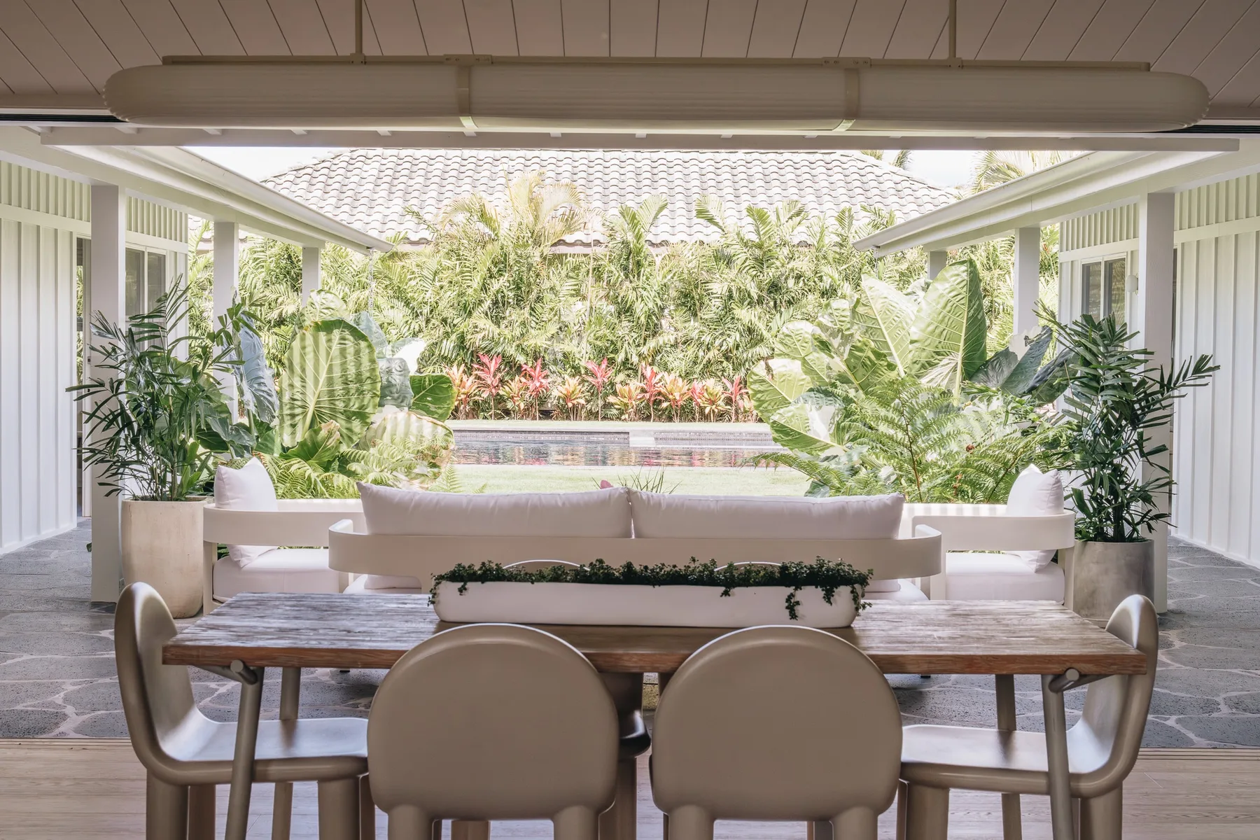 A covered outdoor dining area with a table, seating, and lush tropical plants.