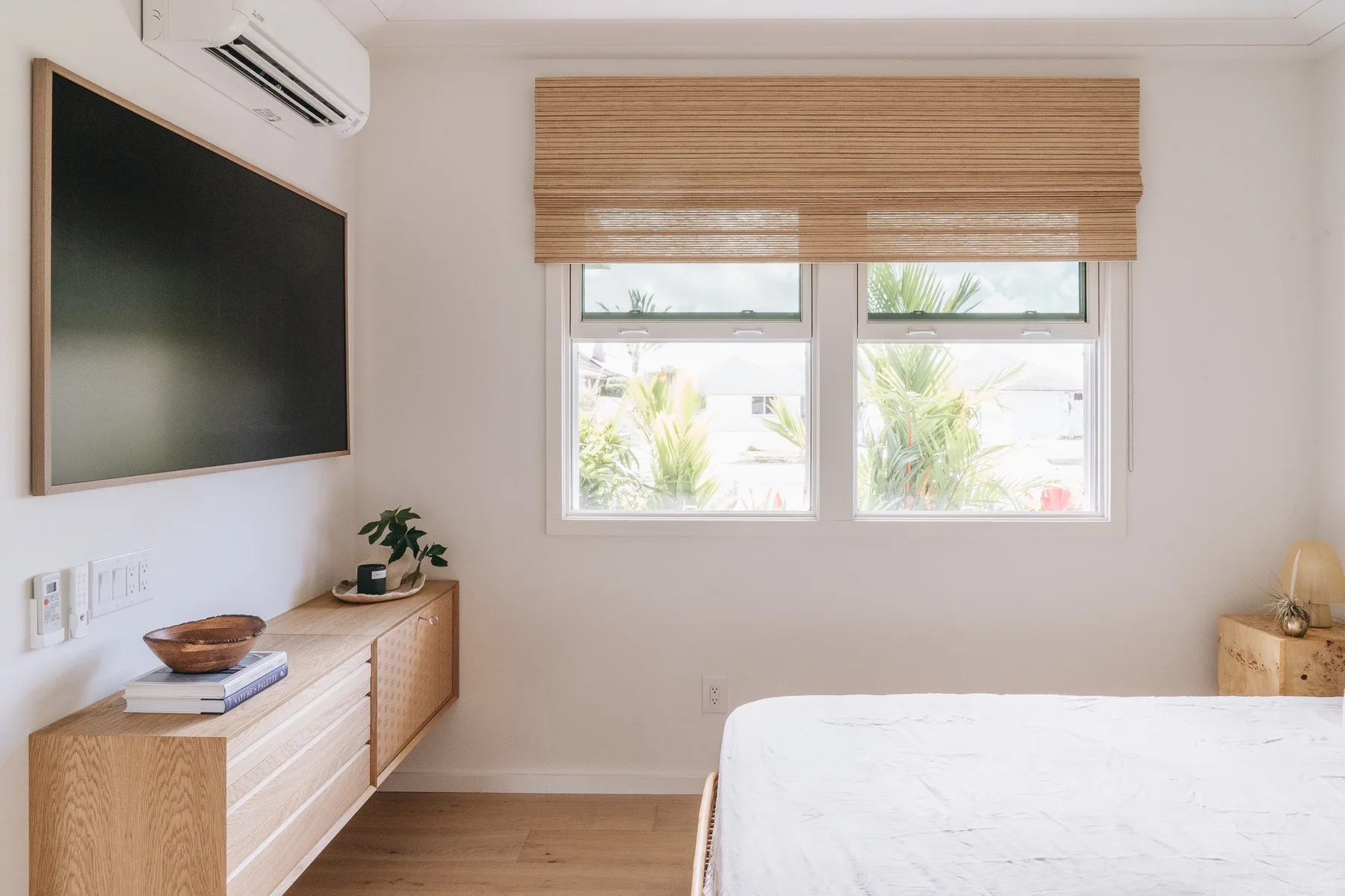A bright bedroom with a bed, windows, and a wooden dresser.