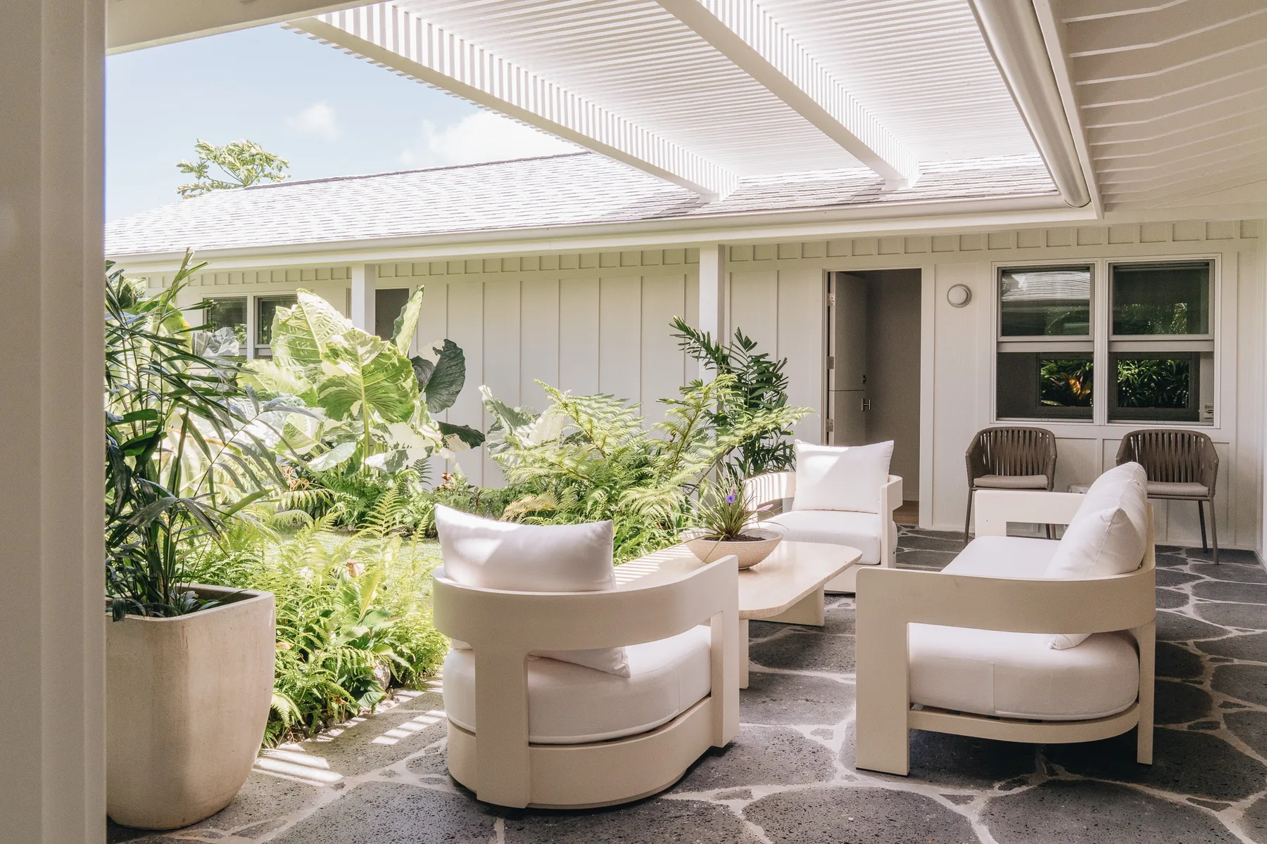 A covered patio with cushioned seating and leafy plants.