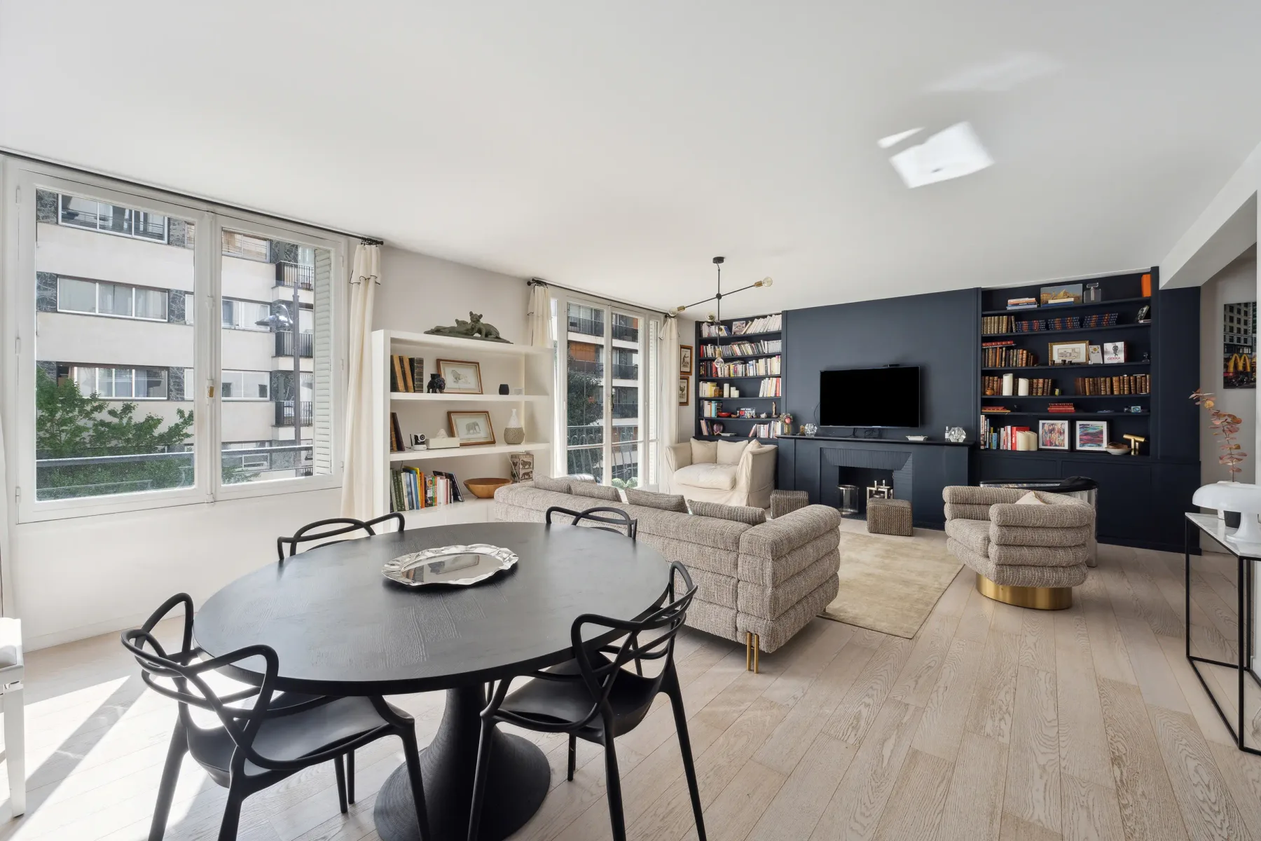 A bright living and dining room with seating, a television, and large windows.