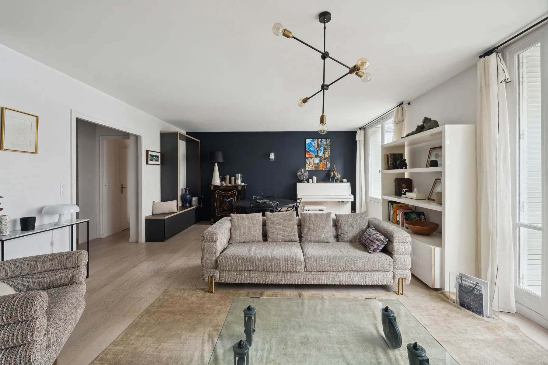 A bright living room with a sofa, glass coffee table, and white piano.