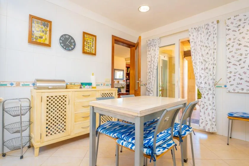 Un comedor luminoso con una mesa, sillas y armarios de tonos claros.