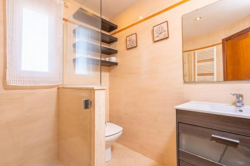 Un baño luminoso con una mampara de vidrio, inodoro y tocador.
