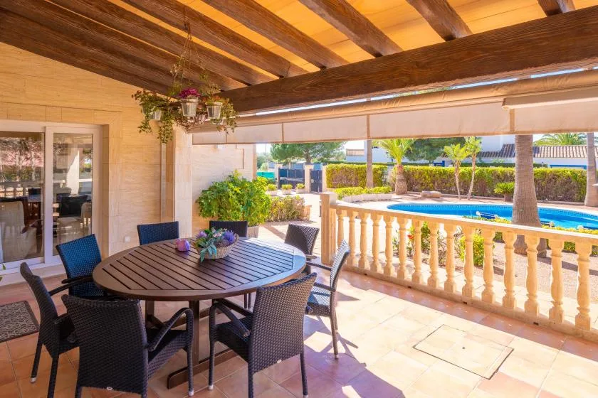 A covered patio dining area opens onto a sunlit pool and garden.