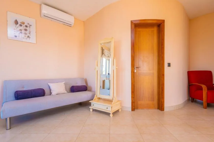 Una sala de estar con un sofá largo, un espejo y una puerta de madera.