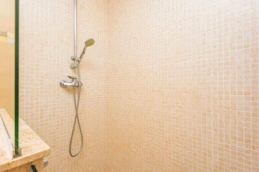 Zona de ducha con azulejos, una ducha fija y una ducha de mano.