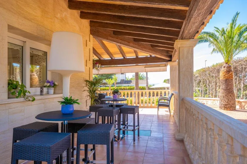 Una zona cubierta de comedor al aire libre con mesas y asientos da a un jardín con palmeras.