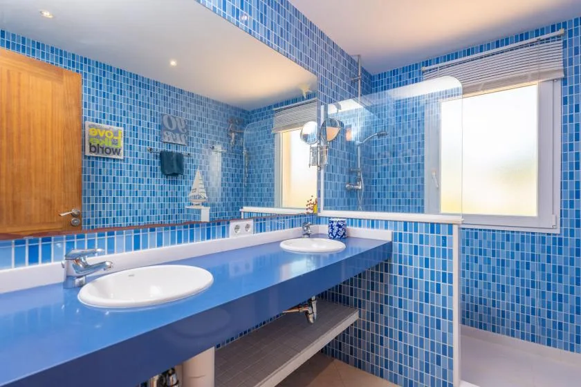 Un baño con azulejos azules, un tocador largo, dos lavabos y una ventana.