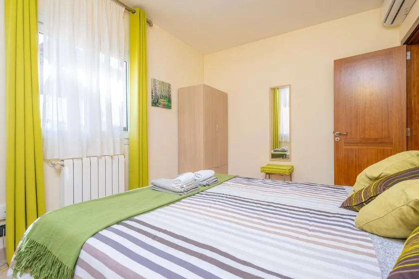 Un dormitorio con una cama a rayas, cortinas verdes y un armario.