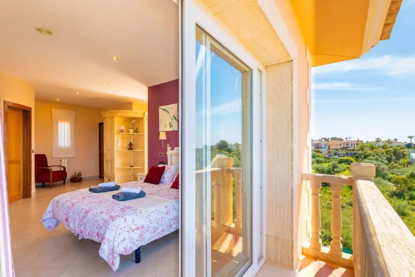 Un dormitorio con una cama junto a un balcón abierto con vistas a zonas verdes.