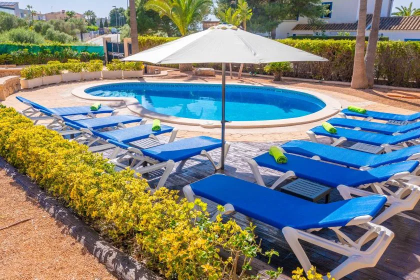 Una piscina está rodeada de tumbonas azules y una sombrilla grande.