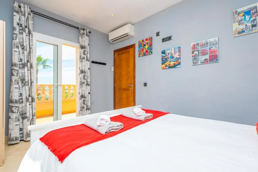Un dormitorio con una cama vestida de blanco y rojo junto a puertas de vidrio.