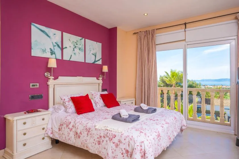 Un dormitorio con una colcha floral y puertas corredizas de vidrio que dan a un balcón.