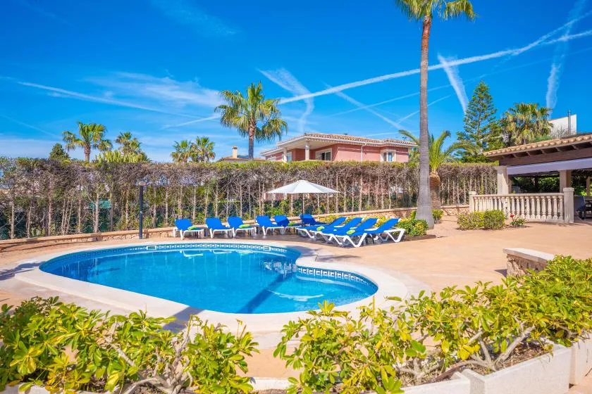 A swimming pool sits beside a paved patio with lounge chairs and an umbrella.