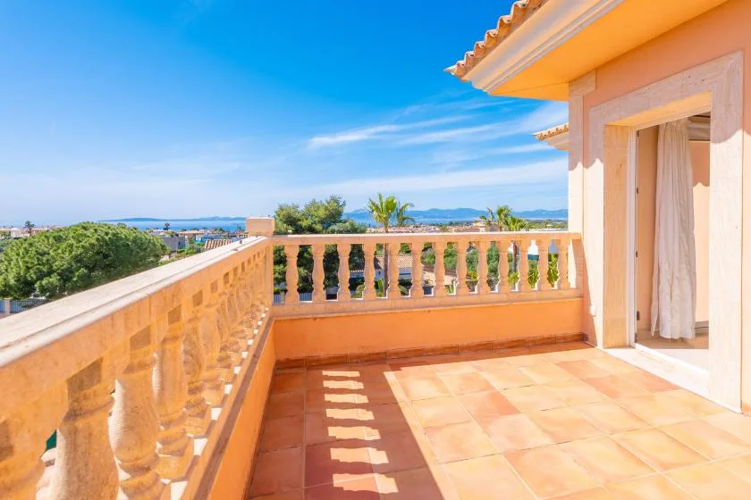 Una terraza soleada con suelo de baldosas y vistas al mar a lo lejos.